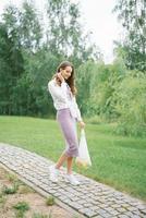 Stylish happy woman walking along a path in a Park and carrying fruit in a mesh bag photo