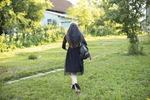 Girl in black dress stands alone on grass. Girl at party. photo