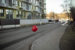 Red balloon flies over road. Object is in air. Color contrast. photo