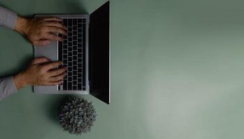 hand using computer laptop and flower on green background.Top view copy space blank. photo