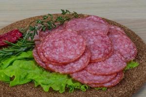 salami en rodajas sobre tablero de madera y fondo de madera foto