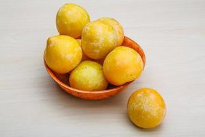 Yellow plums in a bowl on wooden background photo