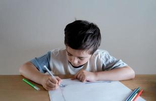 School kid using grey colour pen drawing or sketching on paper,Portrait  boy siting on table doing homework in living room,Child enjoy art and craft activity at home on weekend,Education concept photo