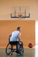 un inválido de guerra en silla de ruedas entrena con una pelota en un club de baloncesto en entrenamiento con equipo deportivo profesional para discapacitados. el concepto de deporte para personas con discapacidad foto