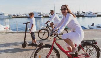 familia feliz disfrutando juntos de una hermosa mañana junto al mar, padres montando en bicicleta y su hijo montando una scooter eléctrica. enfoque selectivo foto