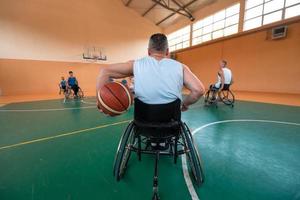 Disabled War veterans mixed race and age basketball teams in wheelchairs playing a training match in a sports gym hall. Handicapped people rehabilitation and inclusion concept photo