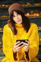 Beautiful European brunette dressed in a yellow woolen sweater and hat outside. The beautiful girl who wears thick stylish autumn clothes in cool weather. photo