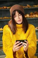 Beautiful European brunette dressed in a yellow woolen sweater and hat outside. The beautiful girl who wears thick stylish autumn clothes in cool weather. photo