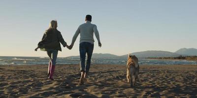 couple with dog having fun on beach on autmun day photo