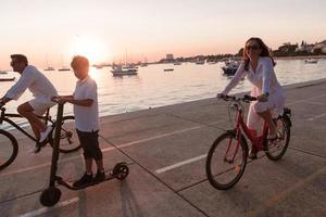 Happy family enjoying a beautiful morning by the sea together, parents riding a bike and their son riding an electric scooter. Selective focus photo