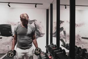 Struggling with age. Confident senior man exercising with dumbbells in health club. Selective focus photo