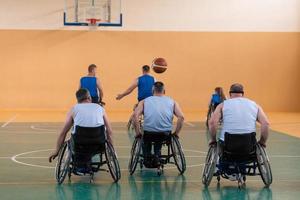 veteranos de guerra discapacitados de raza mixta que se oponen a equipos de baloncesto en sillas de ruedas fotografiados en acción mientras juegan un partido importante en una sala moderna. foto