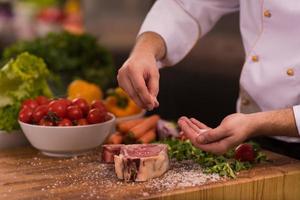 Chef putting salt on juicy slice of raw steak photo