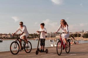 Happy family enjoying a beautiful morning by the sea together, parents riding a bike and their son riding an electric scooter. Selective focus photo