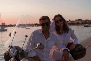 The couple enjoys a vacation while sitting on a scooter by the sea and enjoying the beautiful sunrise. Selective focus photo