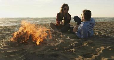 Loving Young Couple Sitting On The Beach beside Campfire drinking beer photo