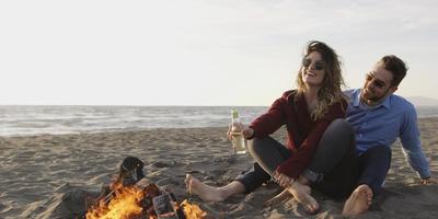 Loving Young Couple Sitting On The Beach beside Campfire drinking beer photo