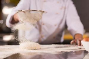 chef sprinkling flour over fresh pizza dough photo