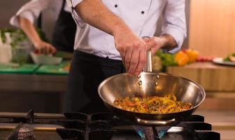 chef putting spices on vegetables in wok photo