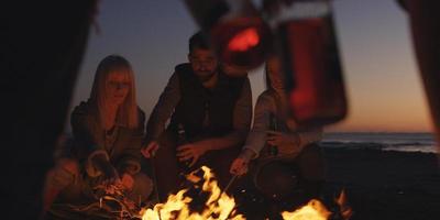 Young Friends Making A Toast With Beer Around Campfire at beach photo