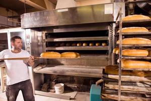 trabajador de panadería sacando panes recién horneados foto