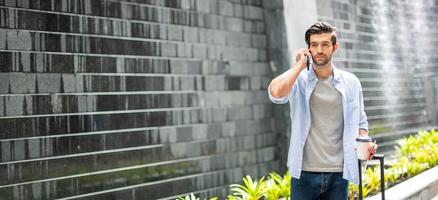 Young caucasian man using smartphone talking and pulling the suitcase waiting his friend for travel together. photo