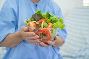 Asian senior or elderly old lady woman patient eating breakfast vegetable healthy food with hope and happy while sitting and hungry on bed in hospital. photo