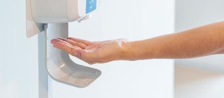 hand spray by automatic sanitizer dispenser in office or apartment. Contactless and Personal hygiene concept photo