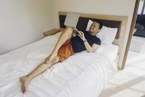 Smiling young man working from the bed. Lying while checking at the laptop. photo