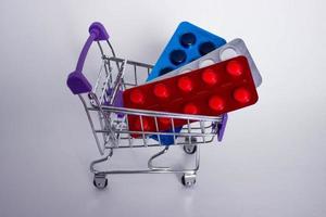 Mini decorative shopping cart with three blisters of tablets on white background. photo