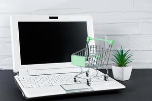 Online sale and Black Friday concept. Laptop and mini shopping cart on white background. photo