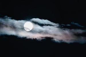 luna llena en el cielo nocturno escondida detrás de las nubes teñidas con la luz del atardecer foto