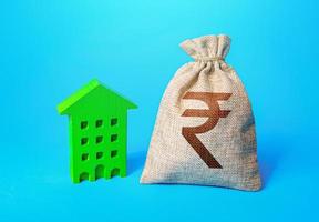 Indian rupee money bag and green Resident building. Investment in green technologies. Reduced emissions and improved energy efficiency. Reducing impact on environment. Investments in housing. photo