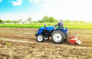 el agricultor en un tractor con fresadora afloja, muele y mezcla el suelo. preparación del campo para la siembra de nuevos cultivos. trabajar en la preparación del suelo para la siembra de semillas de cultivos agrícolas. foto