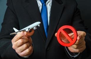 Man is holding an airplane and a red NO sign. Ban on flights. Non-flying zone. Lack of air transporting capacity. Embargo, sanctions. Transport crisis, unprofitable flight routes. Flight cancellation photo