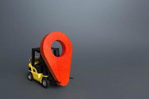 Yellow forklift carries a red location pin pointer. Transportation services and logistics, warehouse management. Real-time tracking of deliveries and goods. Freight infrastructure, redeployment photo