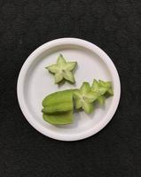 Green star fruit slices on a pink plastic plate isolated on a dark background photo