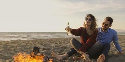 Loving Young Couple Sitting On The Beach beside Campfire drinking beer photo