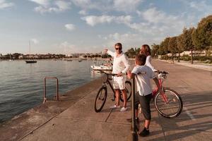 familia feliz disfrutando juntos de una hermosa mañana junto al mar, padres montando en bicicleta y su hijo montando una scooter eléctrica. enfoque selectivo foto