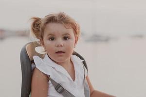 A portrait of a smiling little girl sitting in a bicycle seat. Selective focus photo