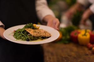 Chef hands holding dish of fried Salmon fish fillet photo