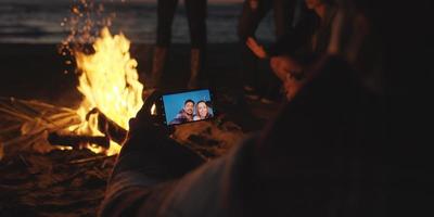 pareja tomando fotos junto a una fogata en la playa