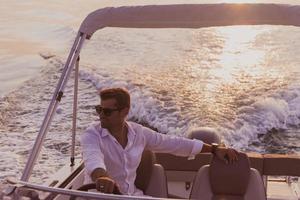 A determined senior businessman in casual clothes and sunglasses enjoys his vacation driving a luxury boat at sunset. Selective focus photo