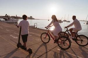 Happy family enjoying a beautiful morning by the sea together, parents riding a bike and their son riding an electric scooter. Selective focus photo