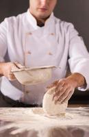 chef sprinkling flour over fresh pizza dough photo