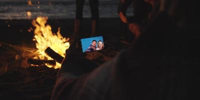 Couple taking photos beside campfire on beach