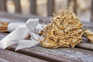 Bouquet of dried roses tied with white ribbon lying on bench at sunset photo