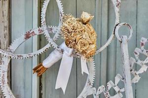 Bouquet of dried roses, tied with white ribbon, in door made of metal gears photo