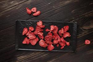 Strawberry chips are stacked in black ceramic tray with dark wooden background. Hundred-percent natural freeze-dried strawberries photo