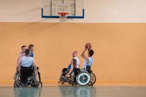 veteranos de guerra discapacitados de raza mixta que se oponen a equipos de baloncesto en sillas de ruedas fotografiados en acción mientras juegan un partido importante en una sala moderna. foto